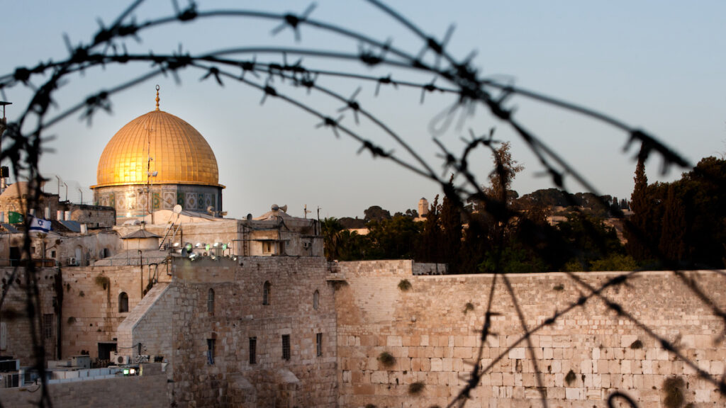 Two of Islam and Judaism's holiest sites, Jerusalem's Dome of the Rock and the Western Wall, seen through barbed wire.